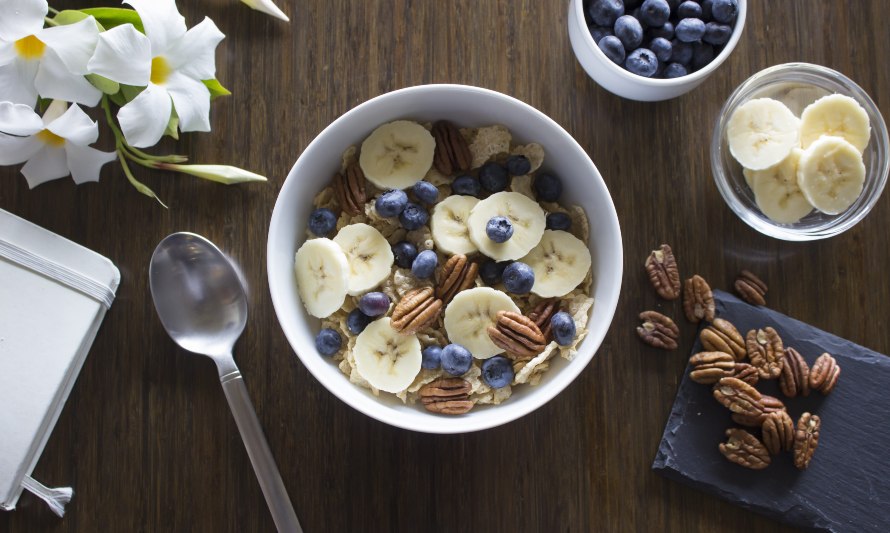 En esta fotografía se puede apreciar un bowl de desayuno con avenas, pecanas, arándanos y plátanos. El plátano es una fruta con alto contenido en vitaminas, minerales, carbohidratos saludables y fibra. 